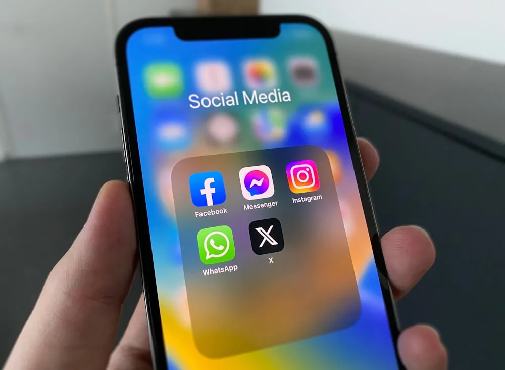 A hand holding a phone showing social media apps